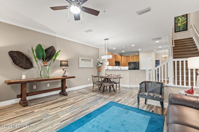 living area with visible vents, baseboards, stairs, ornamental molding, and light wood finished floors