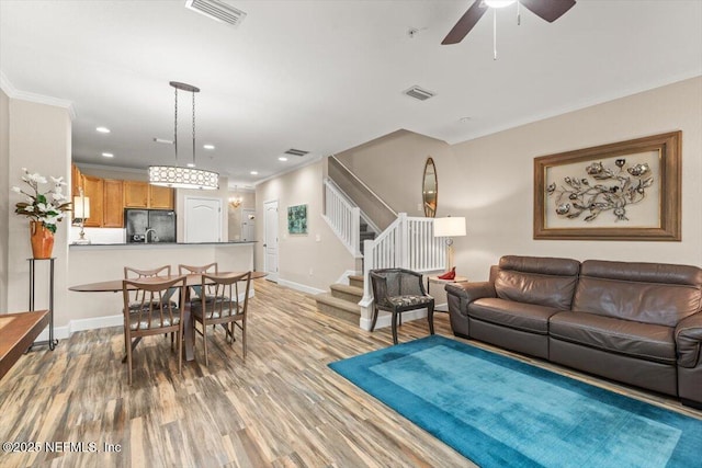 living room featuring stairs, ornamental molding, light wood-type flooring, and visible vents