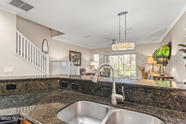 kitchen with visible vents, dark stone counters, open floor plan, crown molding, and a sink