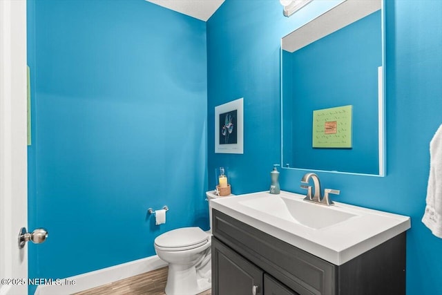 bathroom featuring toilet, baseboards, wood finished floors, and vanity