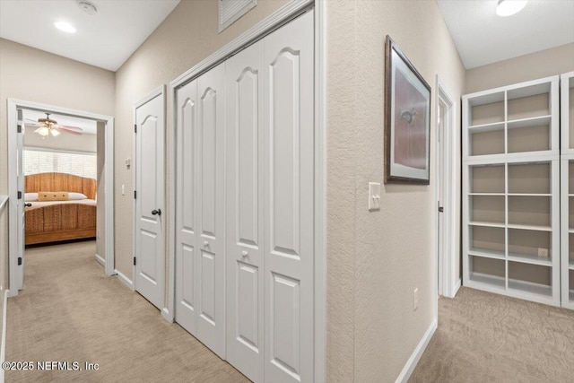 corridor with baseboards, a textured wall, and light colored carpet