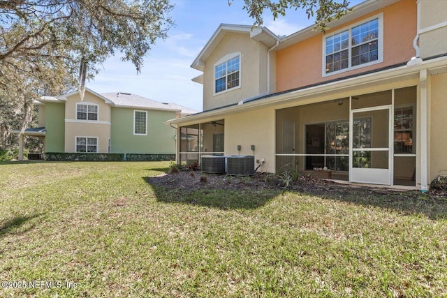 rear view of property featuring a sunroom, central AC unit, a lawn, and stucco siding