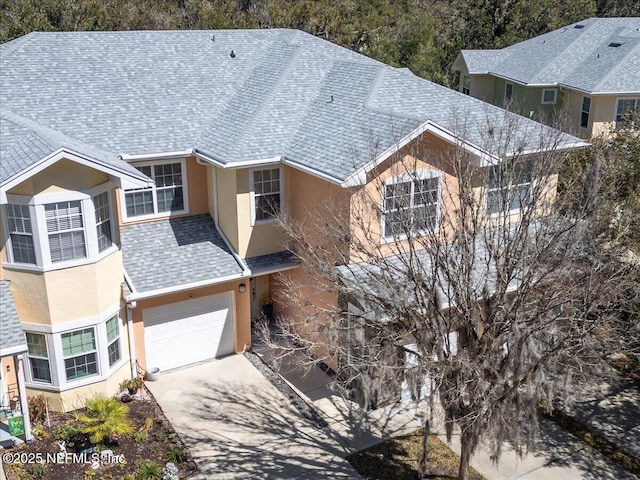 view of front facade with a shingled roof, concrete driveway, a garage, and stucco siding