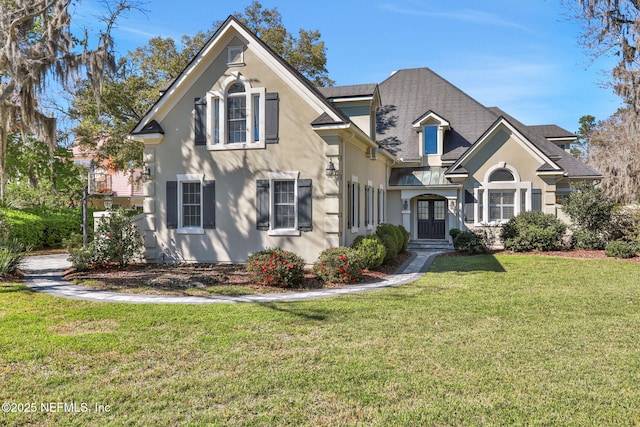 traditional-style home with roof with shingles, a front yard, and stucco siding