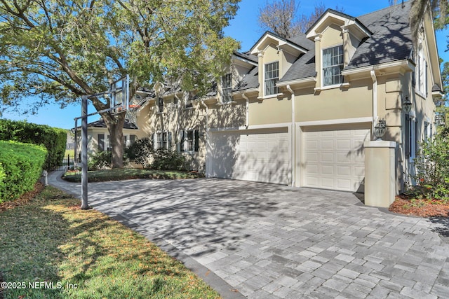 view of front of home with an attached garage, a shingled roof, decorative driveway, and stucco siding