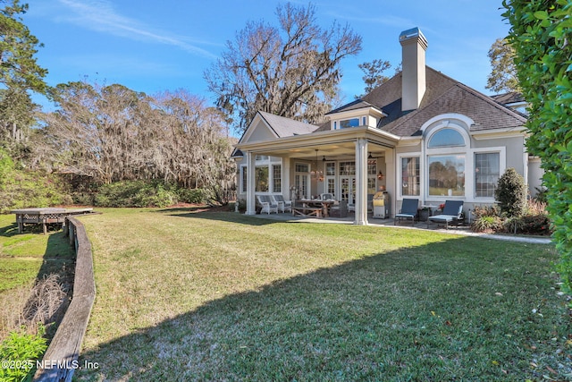 back of house featuring ceiling fan, a yard, roof with shingles, a chimney, and a patio area