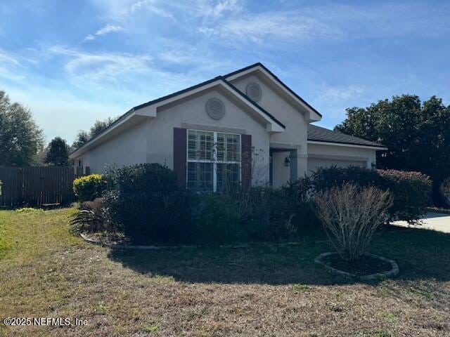 ranch-style home featuring a front lawn, an attached garage, fence, and stucco siding