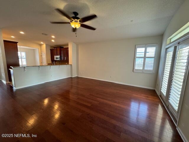 unfurnished living room featuring dark wood-style floors, recessed lighting, a healthy amount of sunlight, and baseboards