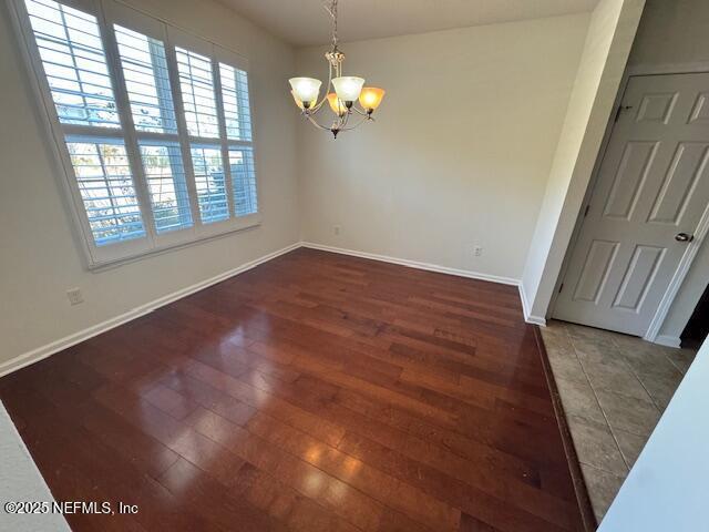 unfurnished dining area featuring a chandelier, baseboards, and wood finished floors