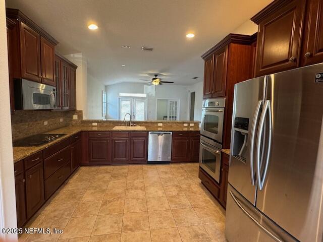 kitchen with a sink, appliances with stainless steel finishes, a peninsula, light tile patterned floors, and light stone countertops