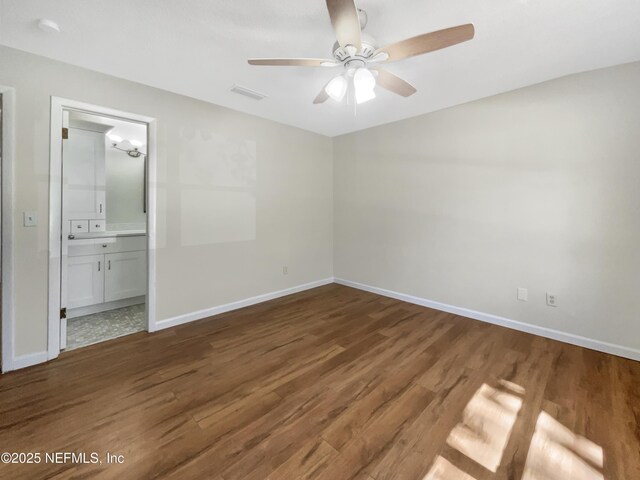 unfurnished bedroom featuring wood finished floors, visible vents, baseboards, ceiling fan, and ensuite bathroom