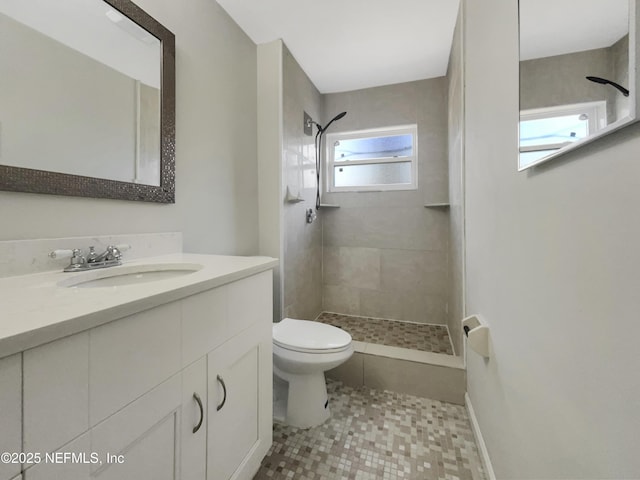 bathroom featuring vanity, toilet, baseboards, and tiled shower