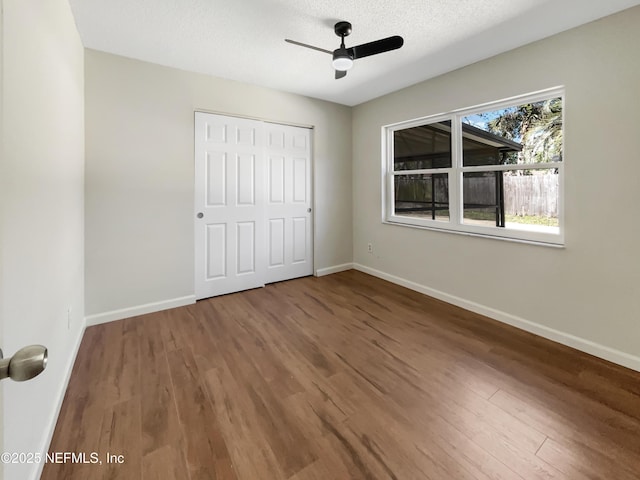 unfurnished bedroom with a textured ceiling, wood finished floors, a closet, baseboards, and ceiling fan