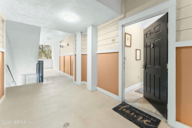 hallway featuring baseboards, a textured ceiling, and an upstairs landing