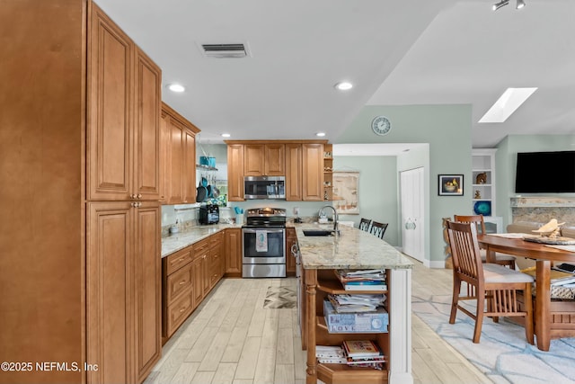 kitchen featuring a sink, appliances with stainless steel finishes, light stone countertops, open shelves, and light wood finished floors