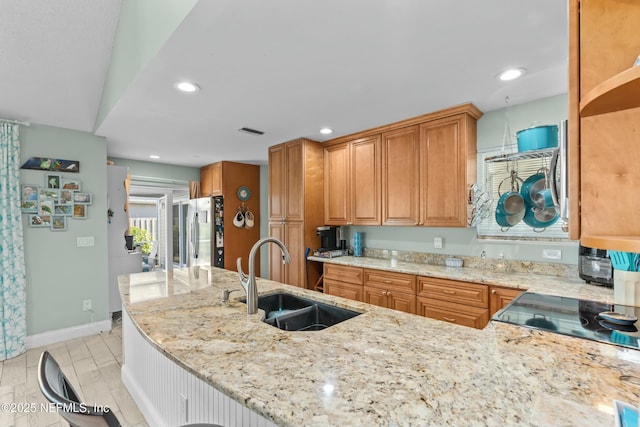 kitchen featuring light stone countertops, brown cabinetry, a sink, and freestanding refrigerator