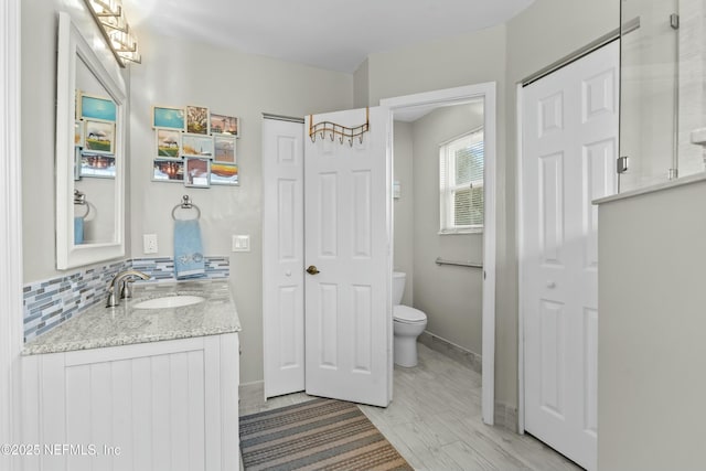 bathroom with baseboards, toilet, wood finished floors, vanity, and backsplash