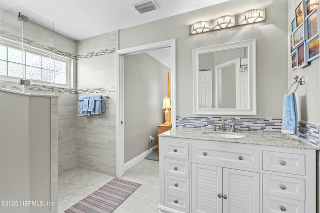 bathroom featuring tasteful backsplash, visible vents, vanity, a walk in shower, and baseboards