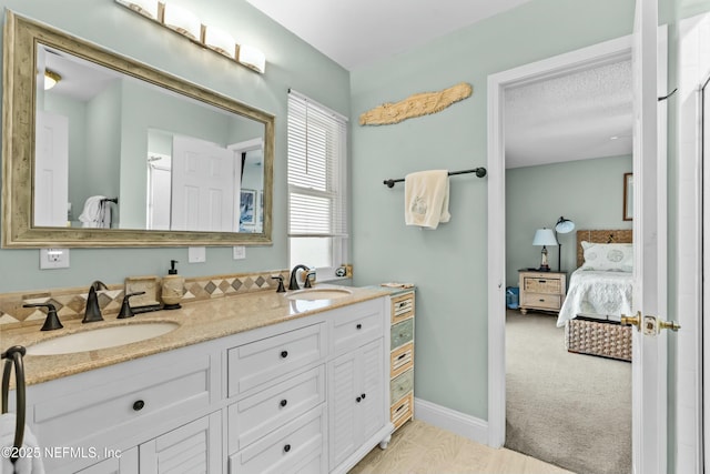 full bathroom with baseboards, double vanity, a sink, and connected bathroom