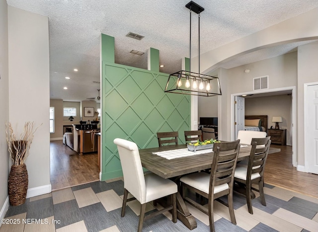 dining area with visible vents, a textured ceiling, wood finished floors, and an accent wall