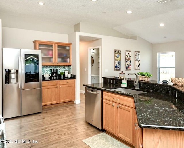 kitchen featuring light wood finished floors, lofted ceiling, a sink, stainless steel appliances, and backsplash