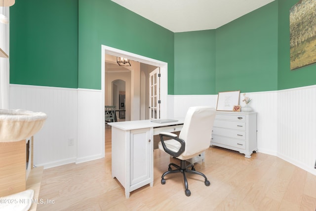 office space with arched walkways, light wood-style flooring, and wainscoting