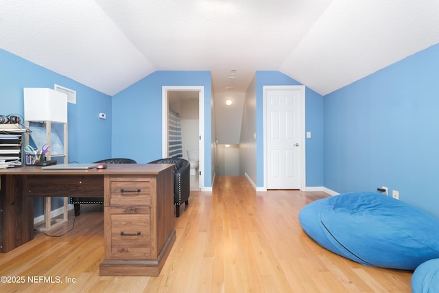 office area with vaulted ceiling, light wood-style flooring, baseboards, and a textured ceiling