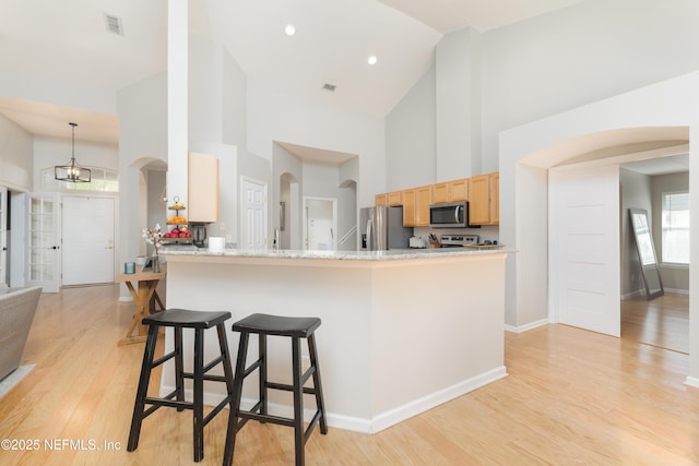 kitchen featuring a breakfast bar, arched walkways, appliances with stainless steel finishes, light wood-type flooring, and a chandelier