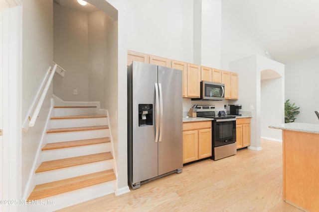 kitchen featuring light brown cabinets, high vaulted ceiling, light wood-style flooring, arched walkways, and stainless steel appliances