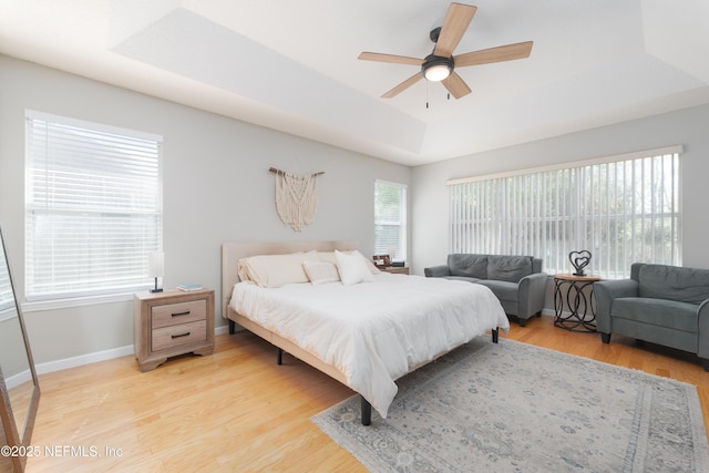 bedroom featuring multiple windows, a raised ceiling, light wood-style floors, and baseboards