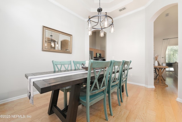 dining space with arched walkways, visible vents, crown molding, and light wood-type flooring