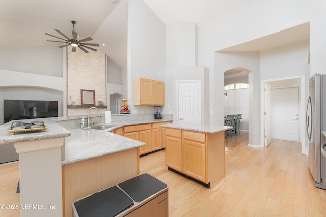 kitchen with light wood-type flooring, light brown cabinetry, a sink, arched walkways, and a peninsula