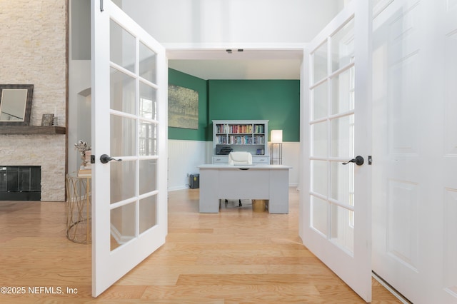 office area featuring a stone fireplace, wood finished floors, and french doors