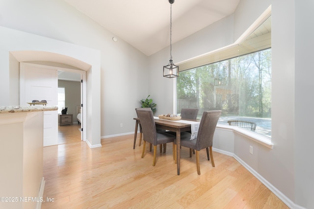 dining space with lofted ceiling, plenty of natural light, light wood-style floors, and arched walkways