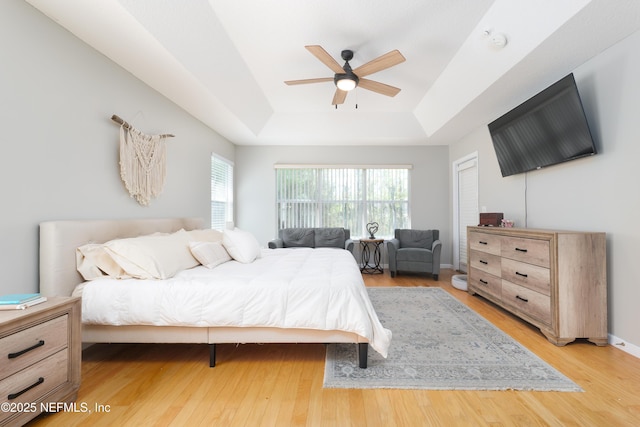 bedroom with a tray ceiling, baseboards, light wood-style floors, and ceiling fan