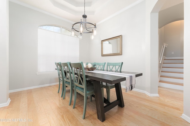 dining room with light wood-type flooring, a tray ceiling, stairway, arched walkways, and an inviting chandelier