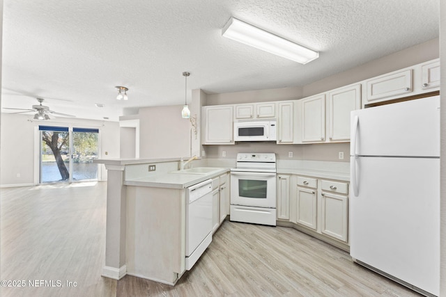 kitchen featuring light countertops, a sink, light wood-type flooring, white appliances, and a peninsula