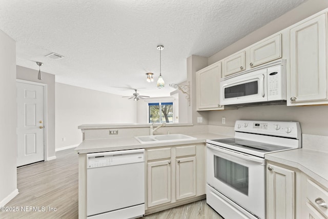 kitchen with a peninsula, white appliances, a sink, visible vents, and light countertops