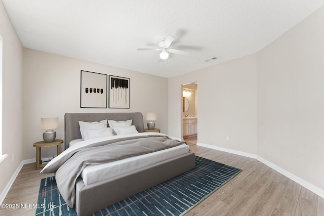 bedroom with a ceiling fan, baseboards, visible vents, light wood-style floors, and ensuite bath