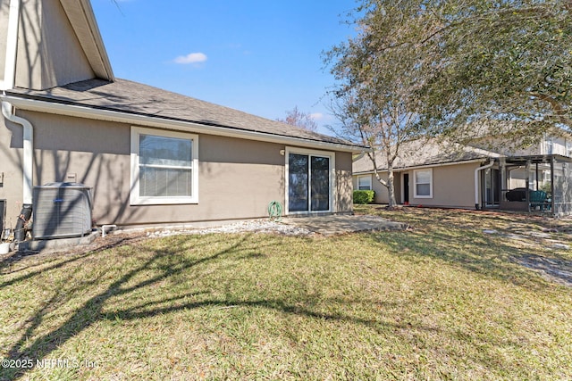 rear view of property featuring a yard, a shingled roof, central air condition unit, and stucco siding