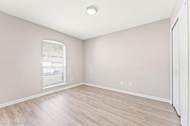 unfurnished bedroom with a textured ceiling, light wood finished floors, a closet, and baseboards