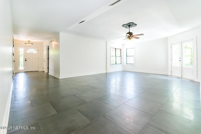 unfurnished living room with a ceiling fan, a wealth of natural light, visible vents, and baseboards