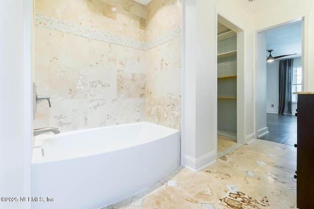 bathroom with ceiling fan, baseboards, a bathing tub, and tile walls