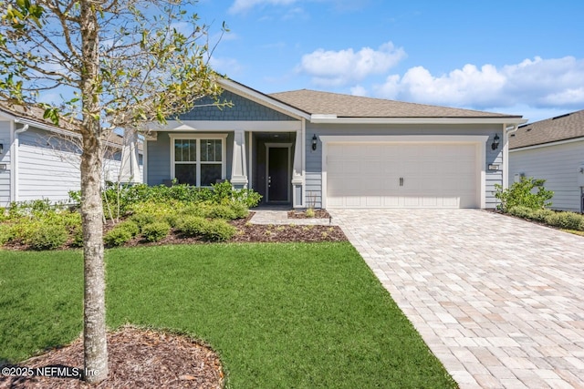 view of front of home featuring a garage, a shingled roof, decorative driveway, and a front yard