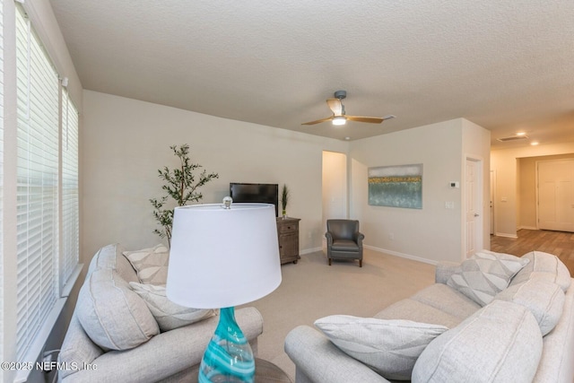 living room with light carpet, ceiling fan, baseboards, and a textured ceiling