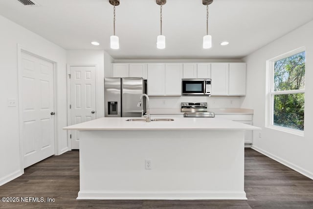 kitchen with light countertops, appliances with stainless steel finishes, white cabinets, a sink, and an island with sink