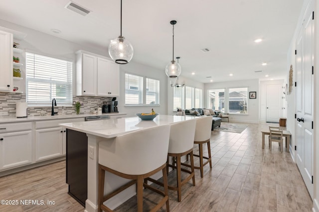 kitchen with light countertops, visible vents, backsplash, a kitchen island, and a sink