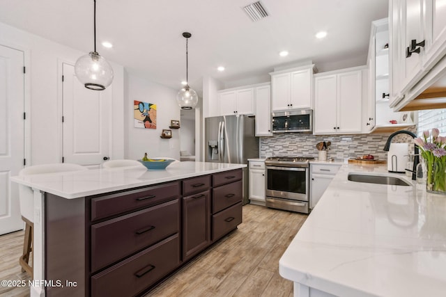 kitchen with visible vents, appliances with stainless steel finishes, white cabinetry, a sink, and dark brown cabinetry