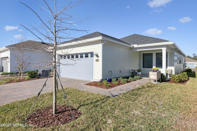 ranch-style house featuring central AC unit, an attached garage, a shingled roof, decorative driveway, and a front lawn