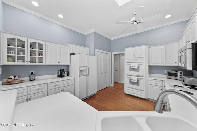 kitchen with white appliances, ornamental molding, a sink, white cabinets, and glass insert cabinets